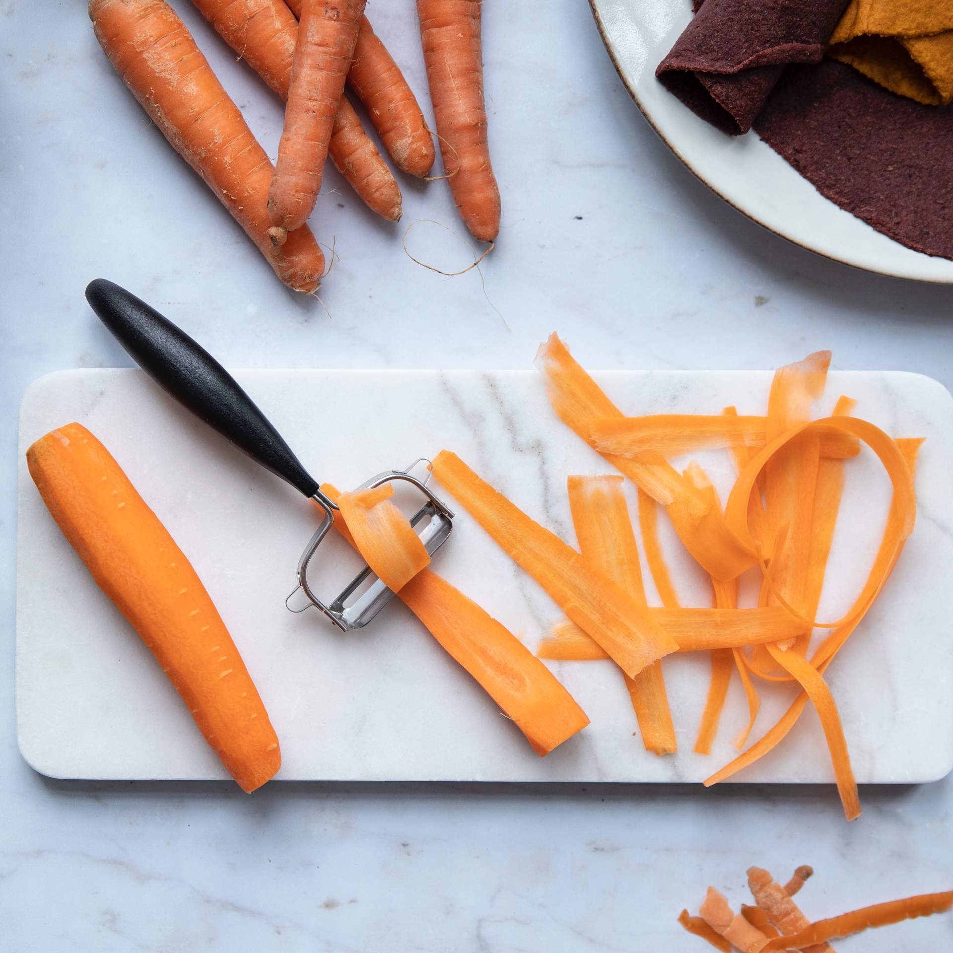 Karotten werden mit einem Sparschäler zu dünnen Streifen geschnitten