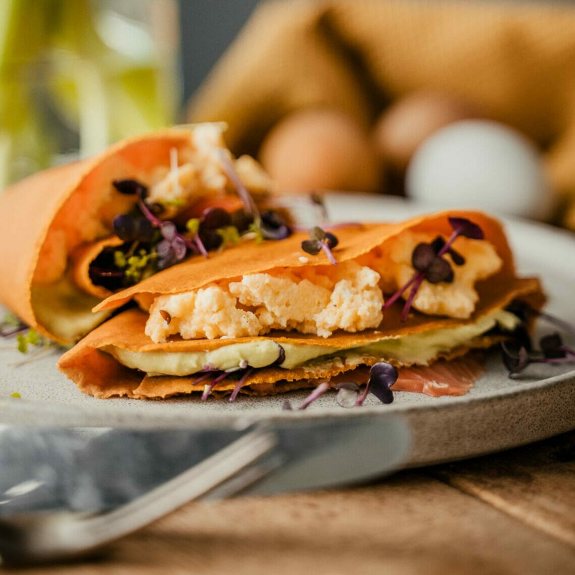 Fertige Karotten Tortilla auf einem Teller gefüllt mir Rührei, Kresse, Avocadomousse und Räucherlachs