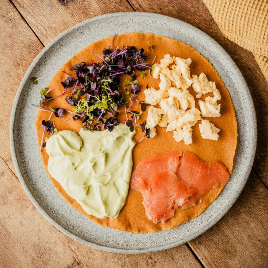 Karotten Tortilla ist zur Hälfte eingeschnitten und belegt, ein Viertel mit Rührei, eines mit Räucherlachs und eines mit Avocadomousse und das letzte mit Kresse