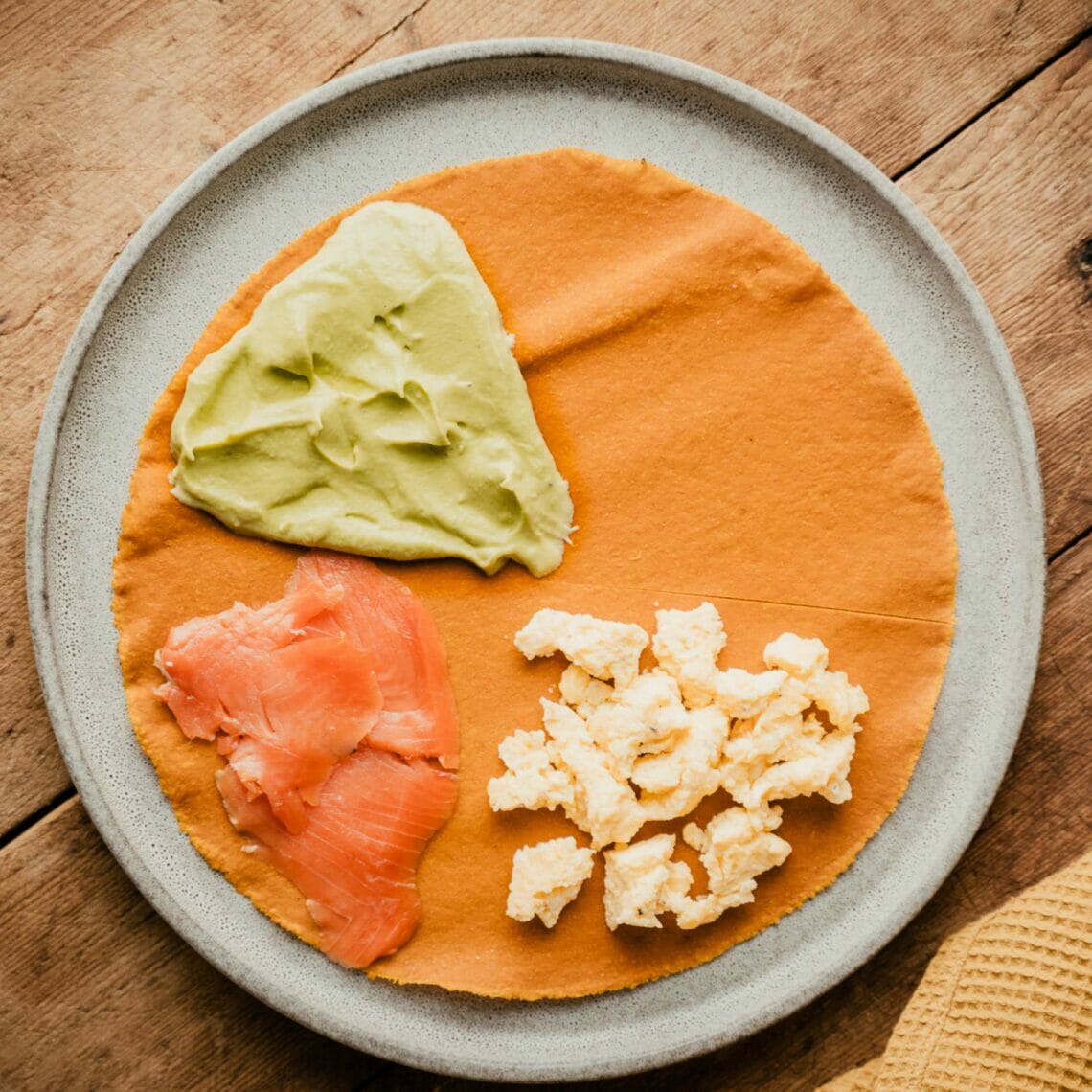 Karotten Tortilla ist zur Hälfte eingeschnitten und zu Dreiviertel belegt, ein Viertel mit Rührei, eines mit Räucherlachs und eines mit Avocadomousse