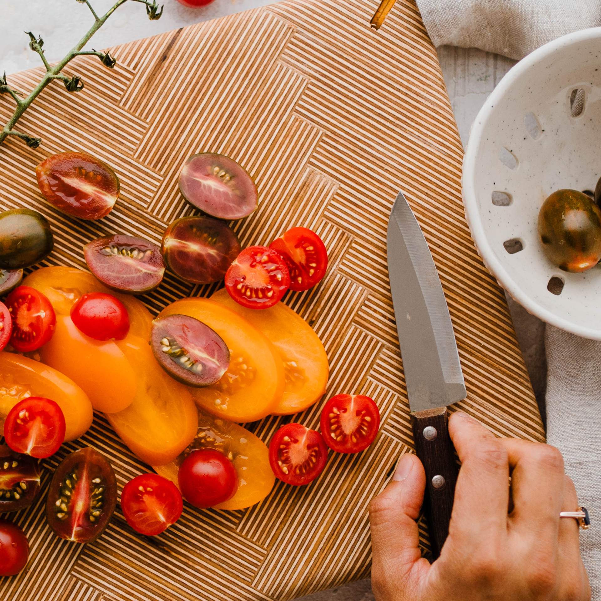 bunte halbierte Tomaten auf einem Schneidebrett, Messer wird in Hand gehalten