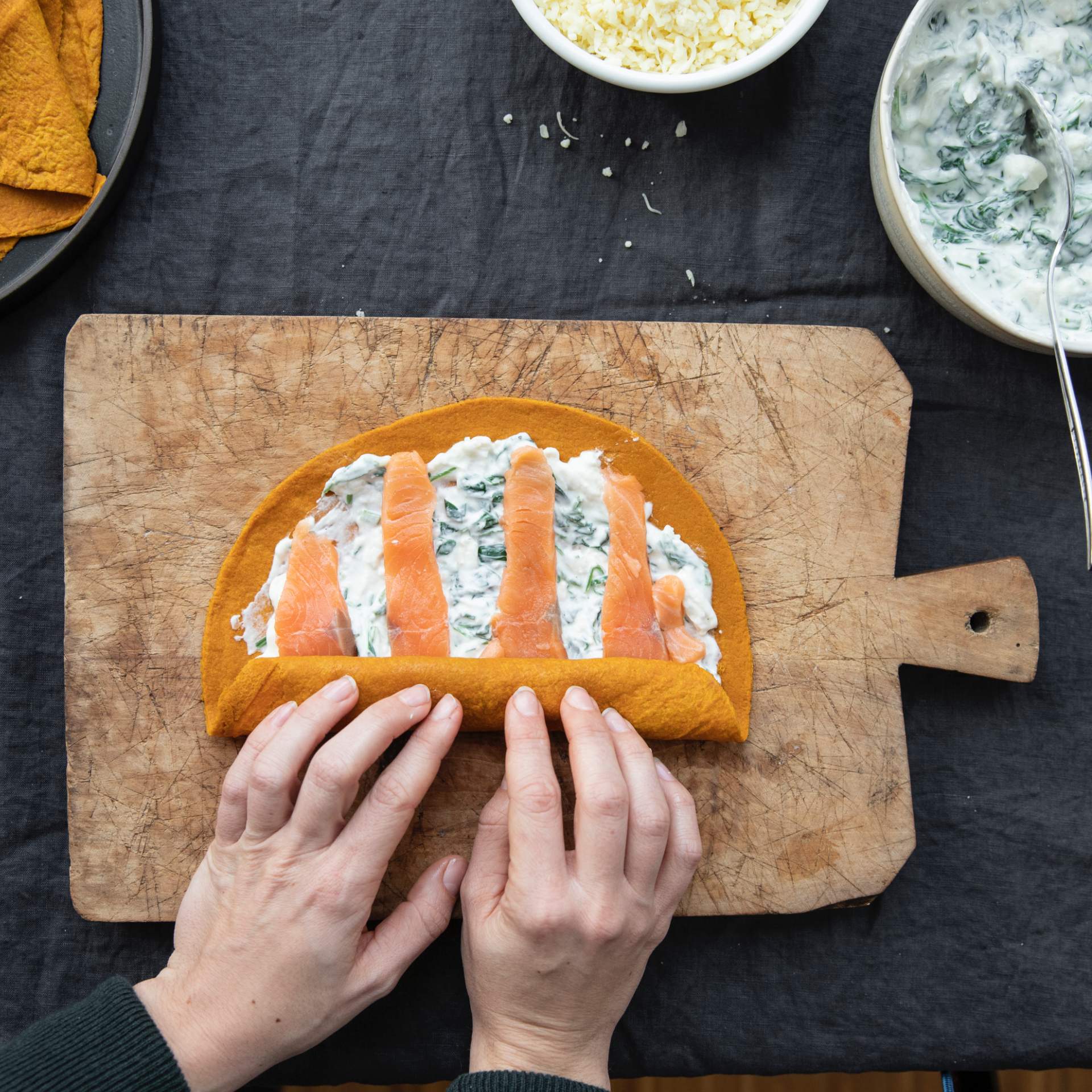 Karotten Tortilla Wrap gefüllt mit Lachstreifen, Spinat und Ziegenkäse wird zusammen gerollt