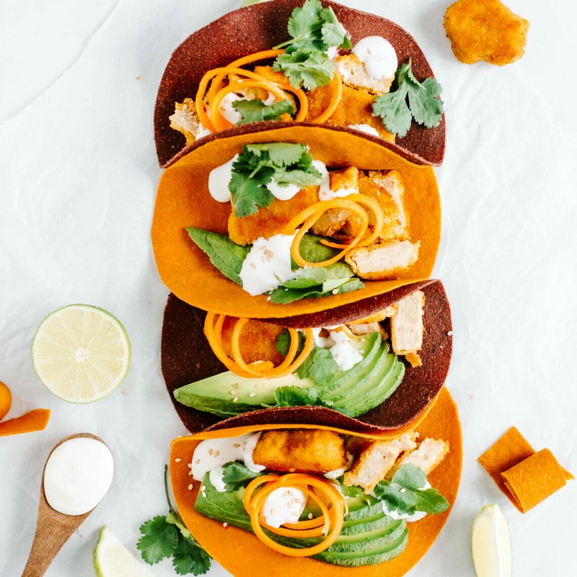 Vier Karotten und Rote Beete Tortillas als Tacos befüllt mit veganen Chicken Nuggets, Avocado und veganer Mayonnaise getoppt mit Sesam