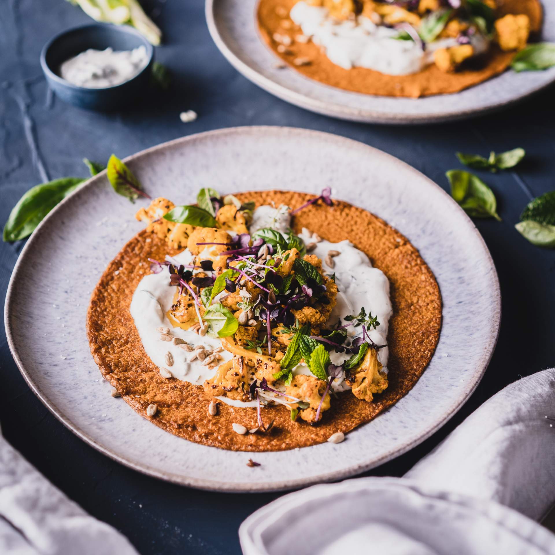Tortilla belegt mit Minzjoghurt, Blumenkohl und frischen Kräutern auf einem Teller