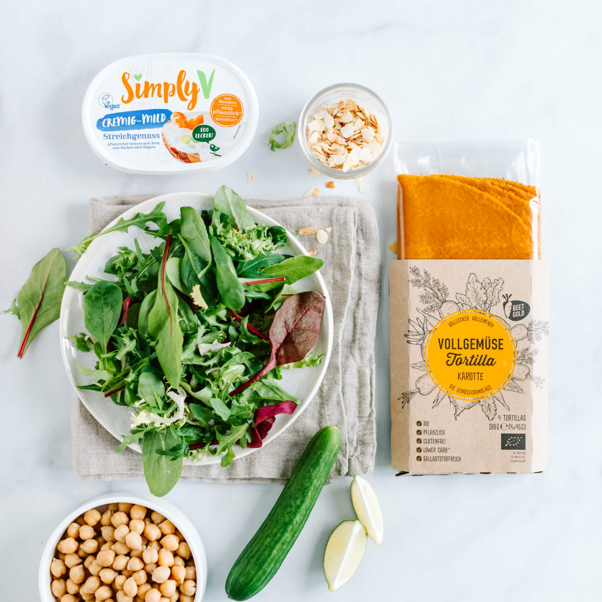 Zutaten für ein Wrap Rezept: Karotten Tortilla Verpackung, veganer Frischkäse, Mandeln, Kichererbsen, Gurke, Limette und gemischter Salat