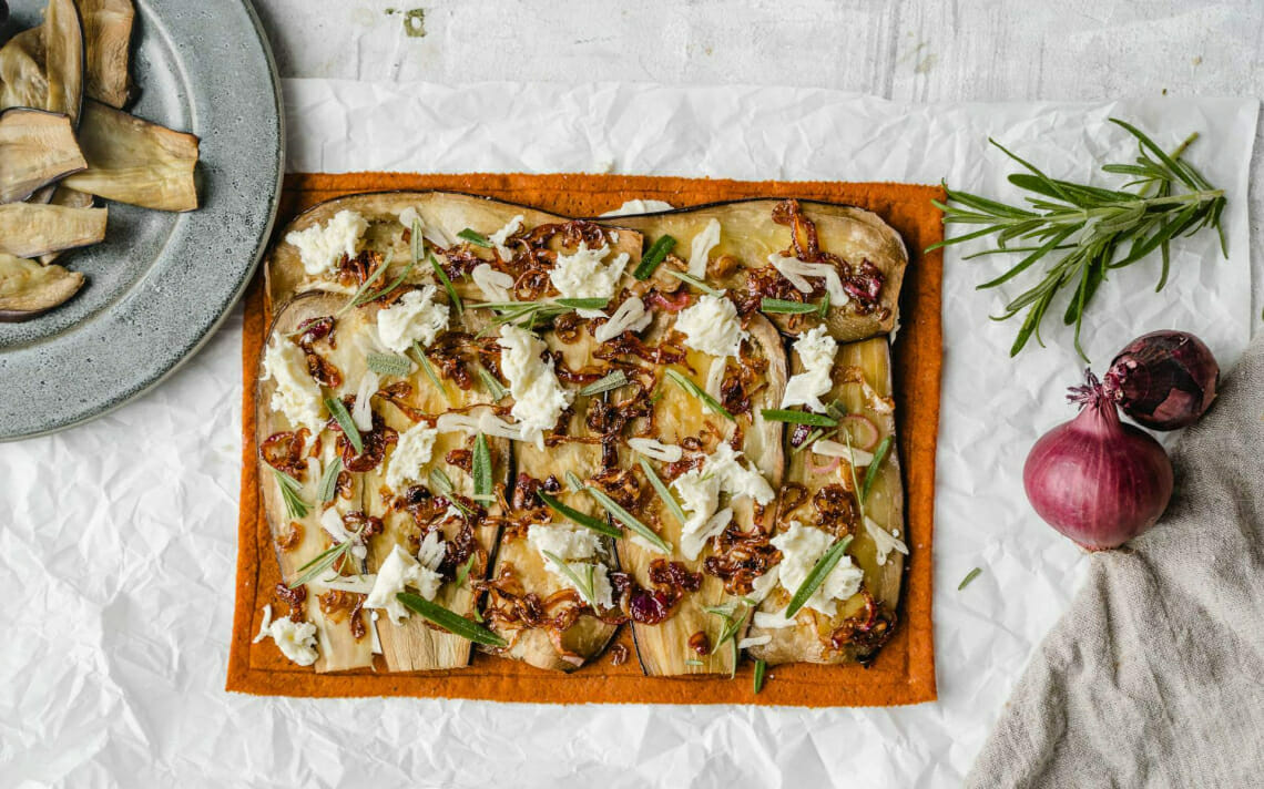 Ungebackener Gemüse Pizzaboden belegt mit Mozzarella, Auberginen, Zwiebeln und Rosmarin
