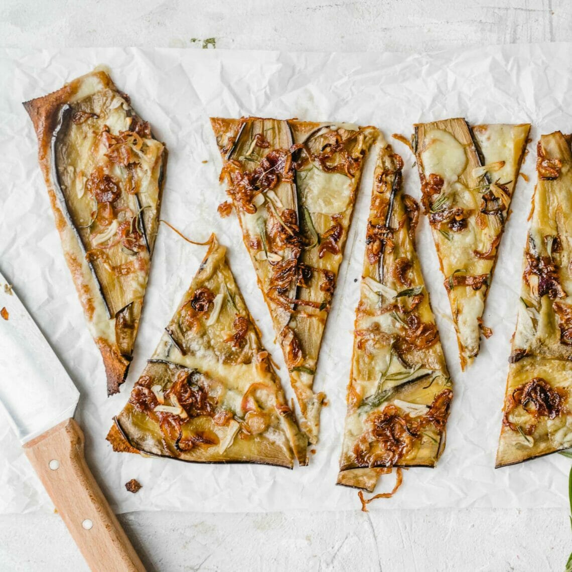 In Dreiecke geschnittene Pizza belegt mit Aubergine, Balsamicozwiebeln und Rosmarin