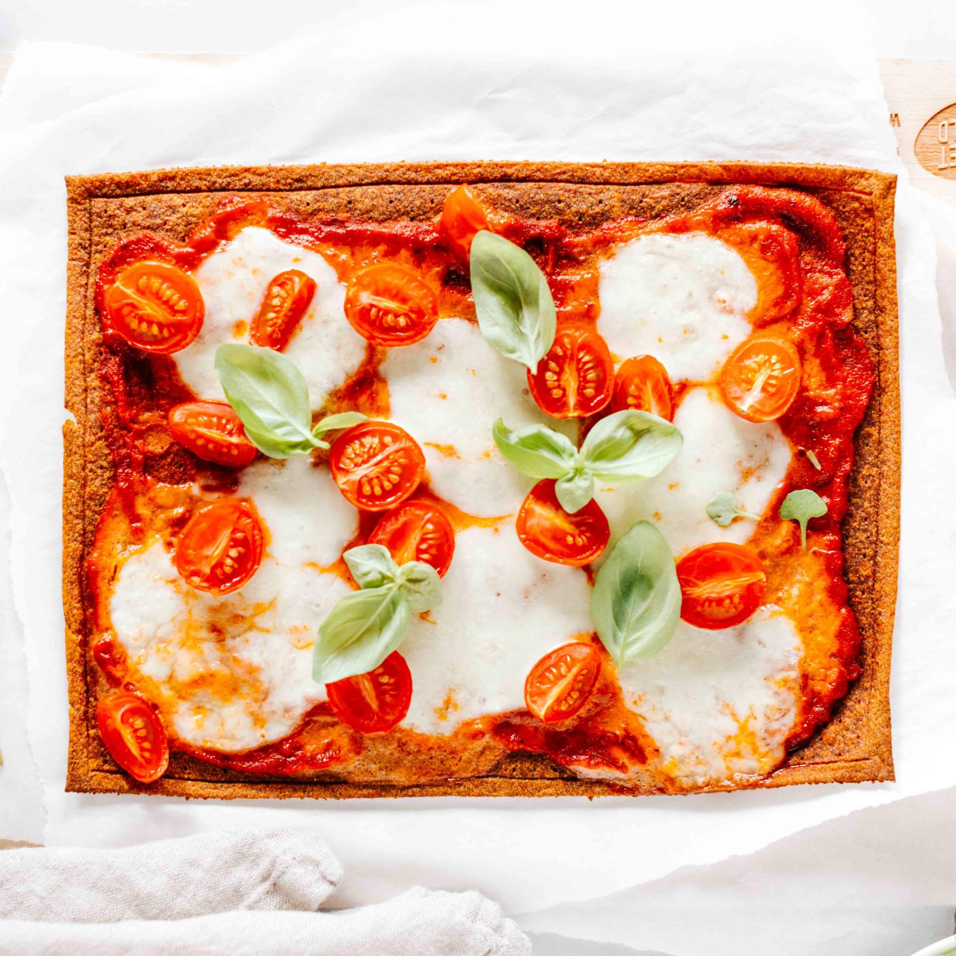 Fertige Pizza Margherita mit einem Gemüse Pizzaboden auf einem Holzbrett