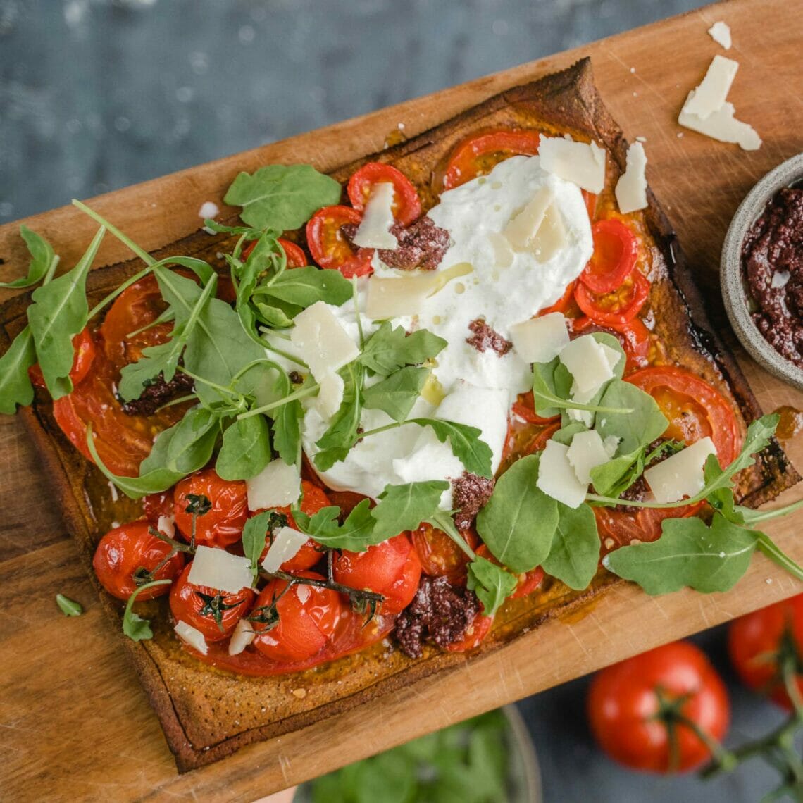 Gebackener Pizzaboden belegt mit Tomaten, Cocktailtomaten, getrockneten Tomaten, Rucola, Burrata und Parmesan