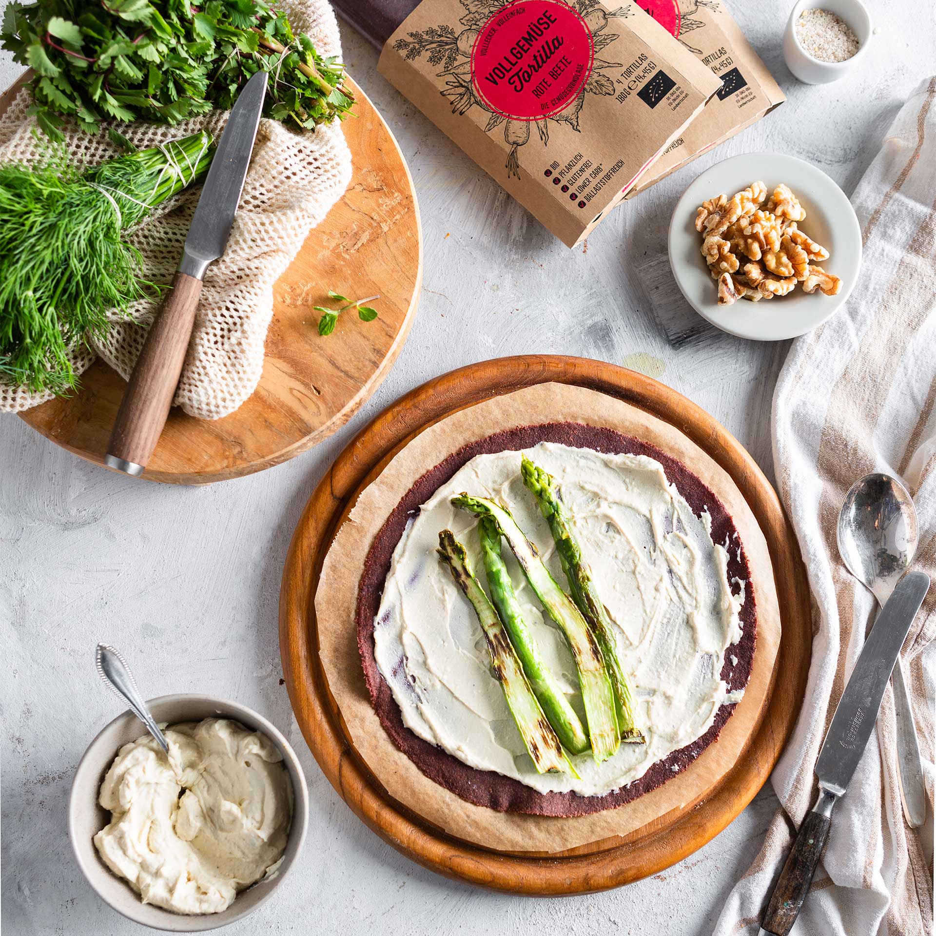 Rote Beete Tortilla Wrap auf rundem Holzbrett bestrichen mit Käsecreme und in der Mitte belegt mit Spargel