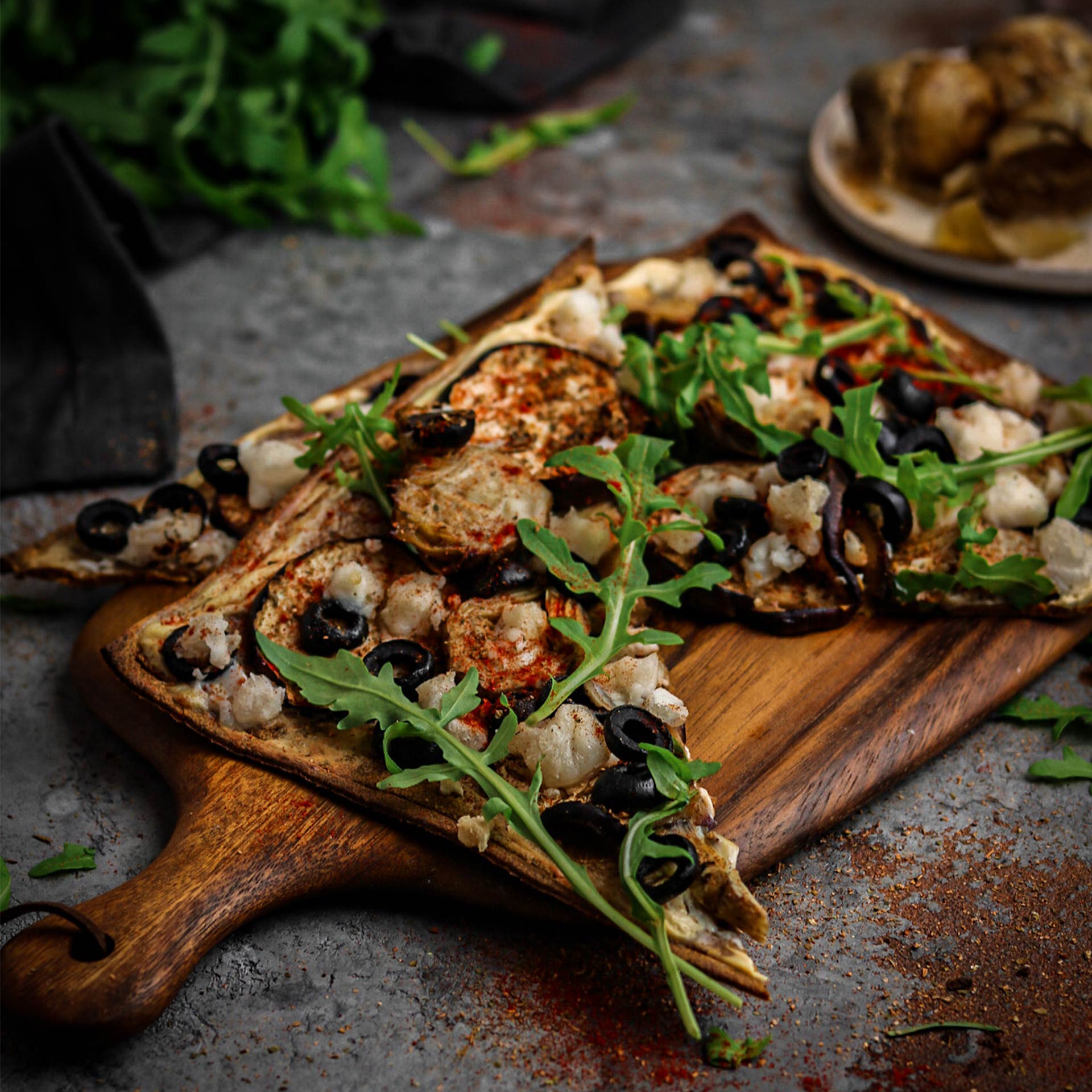 Geschnittenes Pizzastück auf Holzbrett mit Artischocken, Oliven, Aubergine und Rucola