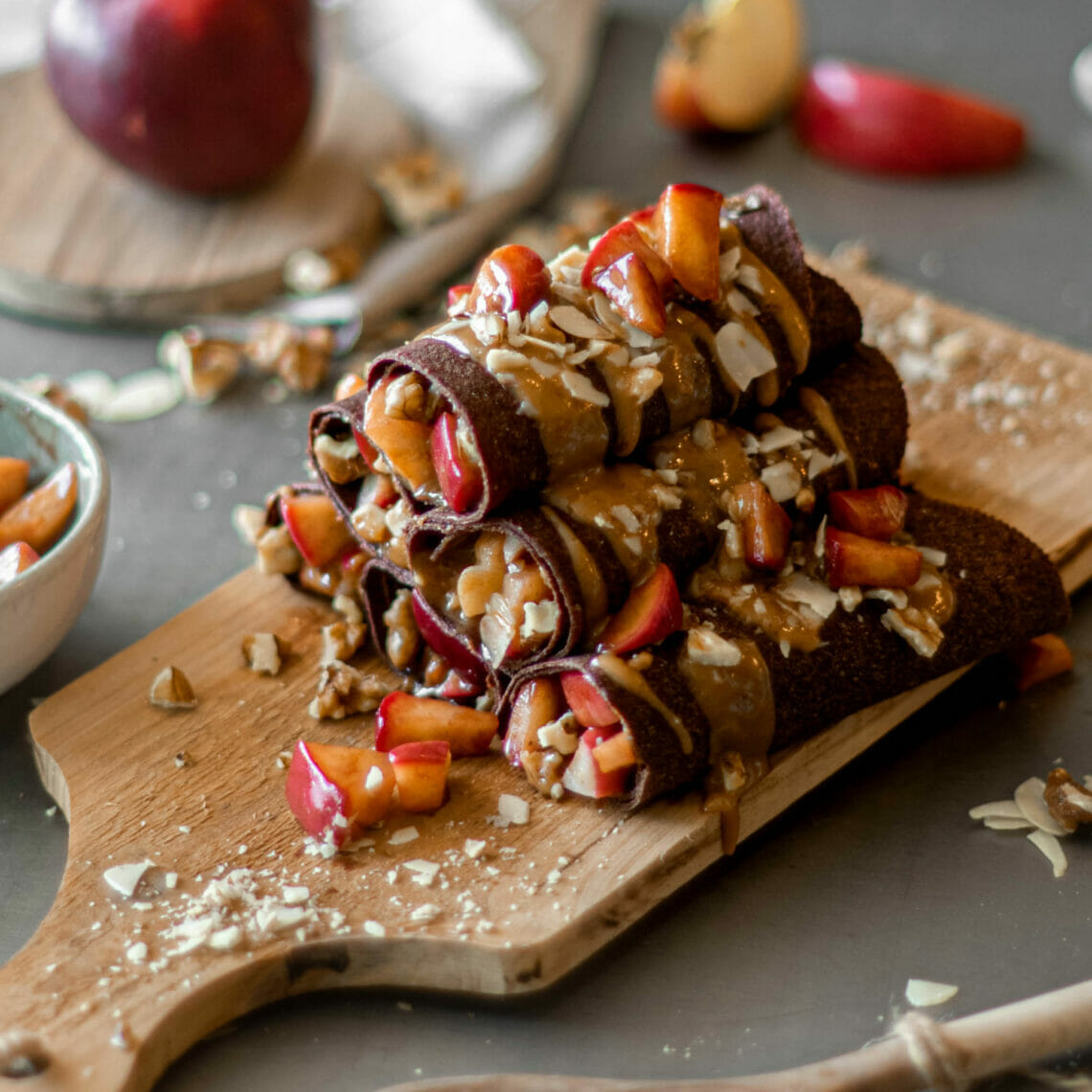 Eingerollte Rote Beete Tortilla Wraps als Crêpes auf Holzbrett mit Apfelfüllung und Mandel, Karamell Topping