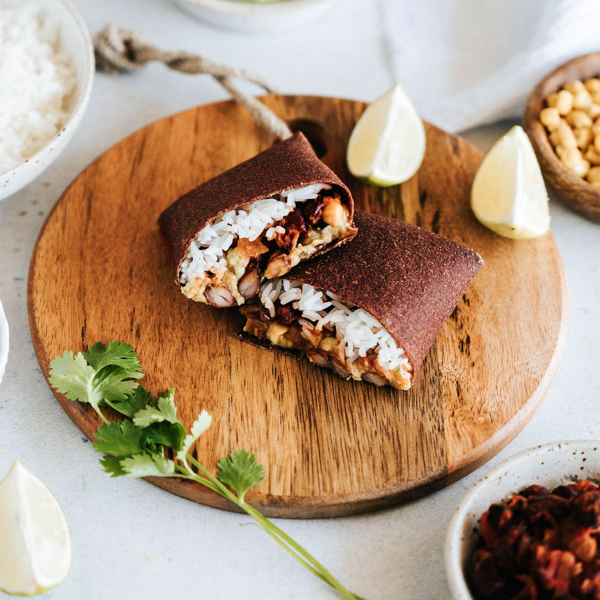 Rote Beete Tortilla Wrap gerollt als Burrito gefüllt mit Reis, Bohnen, Tomaten und Gucamole halbiert auf einem Holzbrett