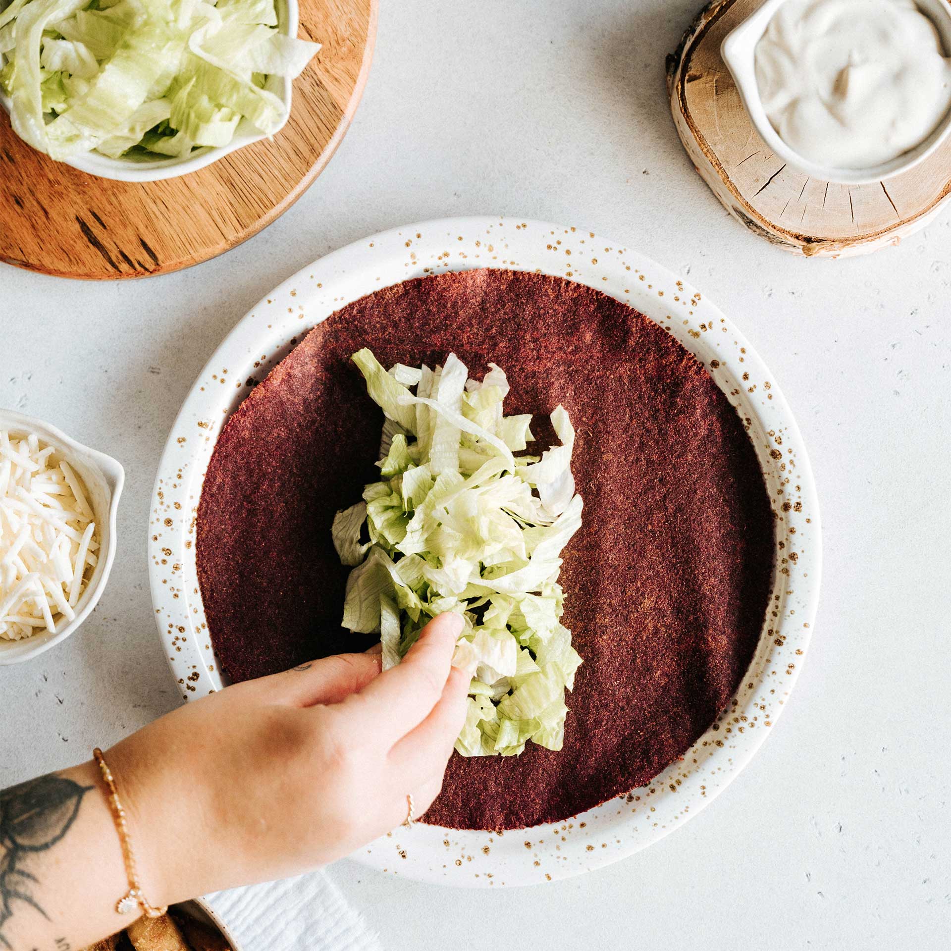 Salat wird auf einen Rote Beete Tortilla Wrap gegeben der auf einem Teller liegt