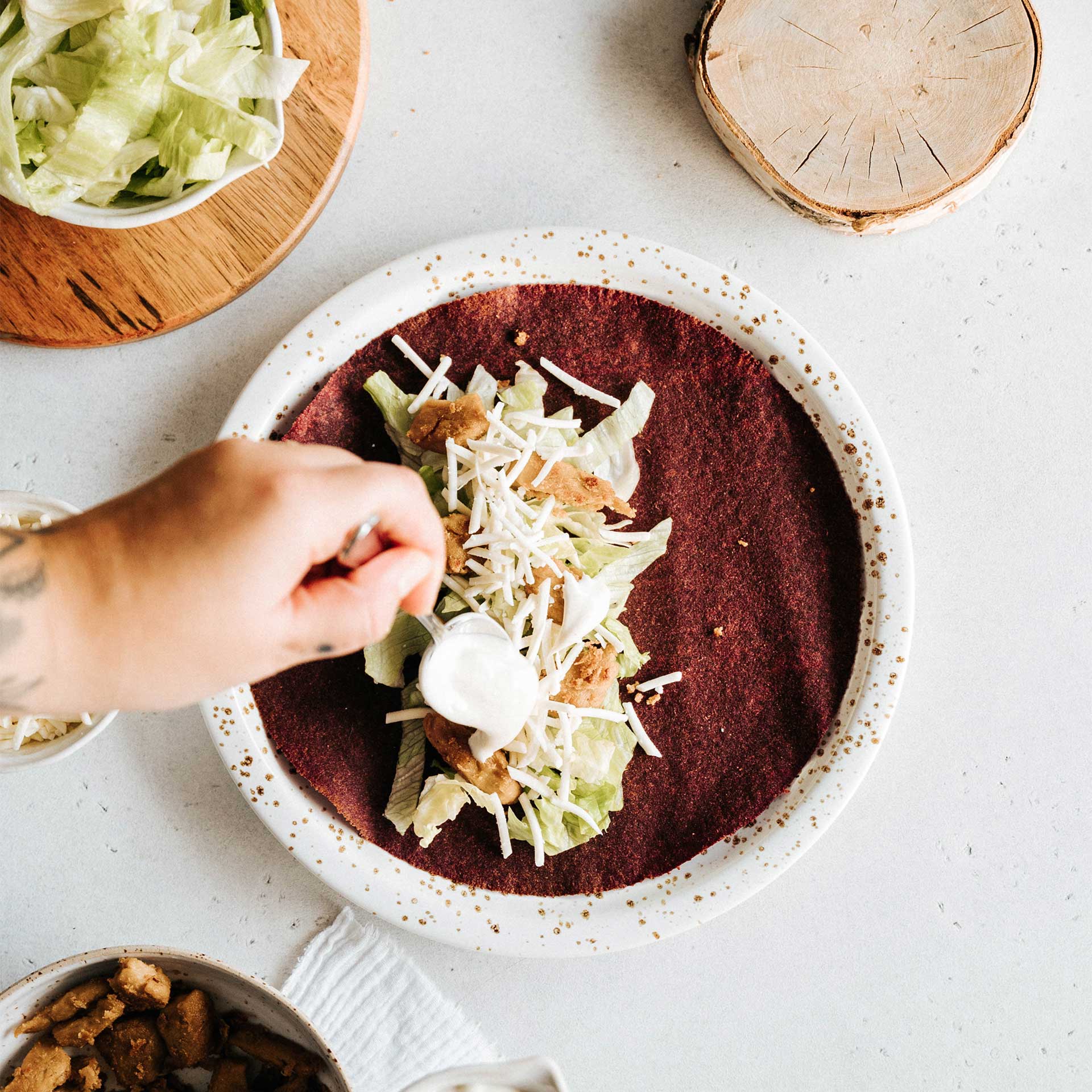 Sauce wird auf einen mit Salat, veganem Käse und veganem Hänchen belegen Tortilla Wrap gegeben