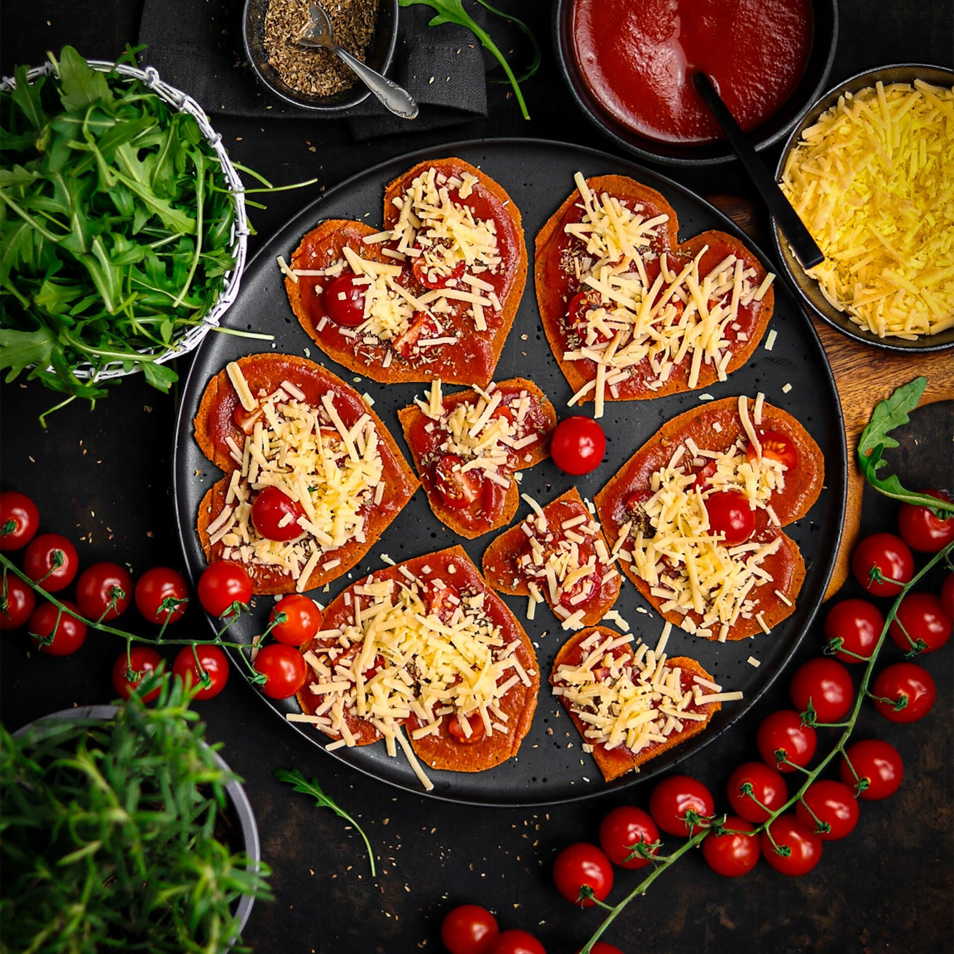 Herzen aus Pizzaboden mit Tomatensauce belegt mit Cocktailtomaten und Käse