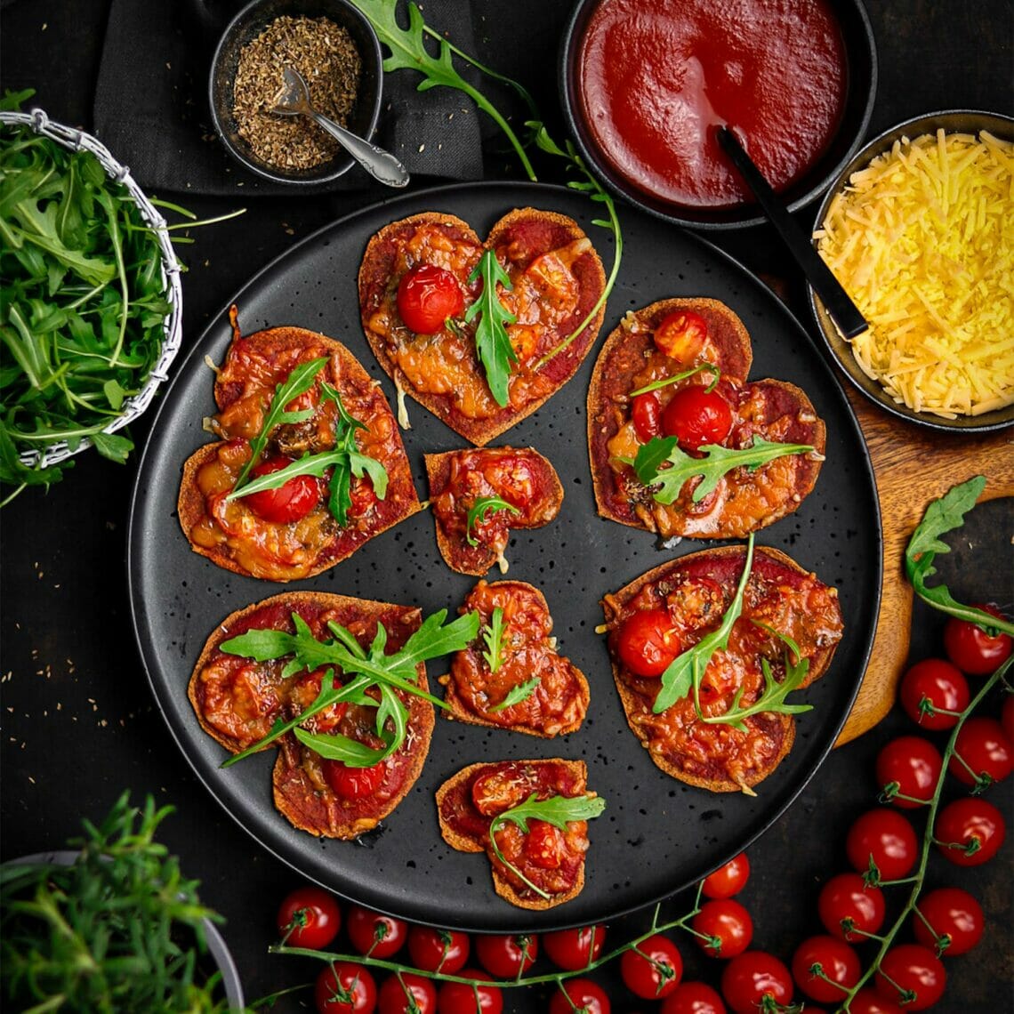 kleine Pizzas in Form von Herzen, mit Tomatensauce, Cocktailtomaten überbacken mit Käse und garniert mit Rucola