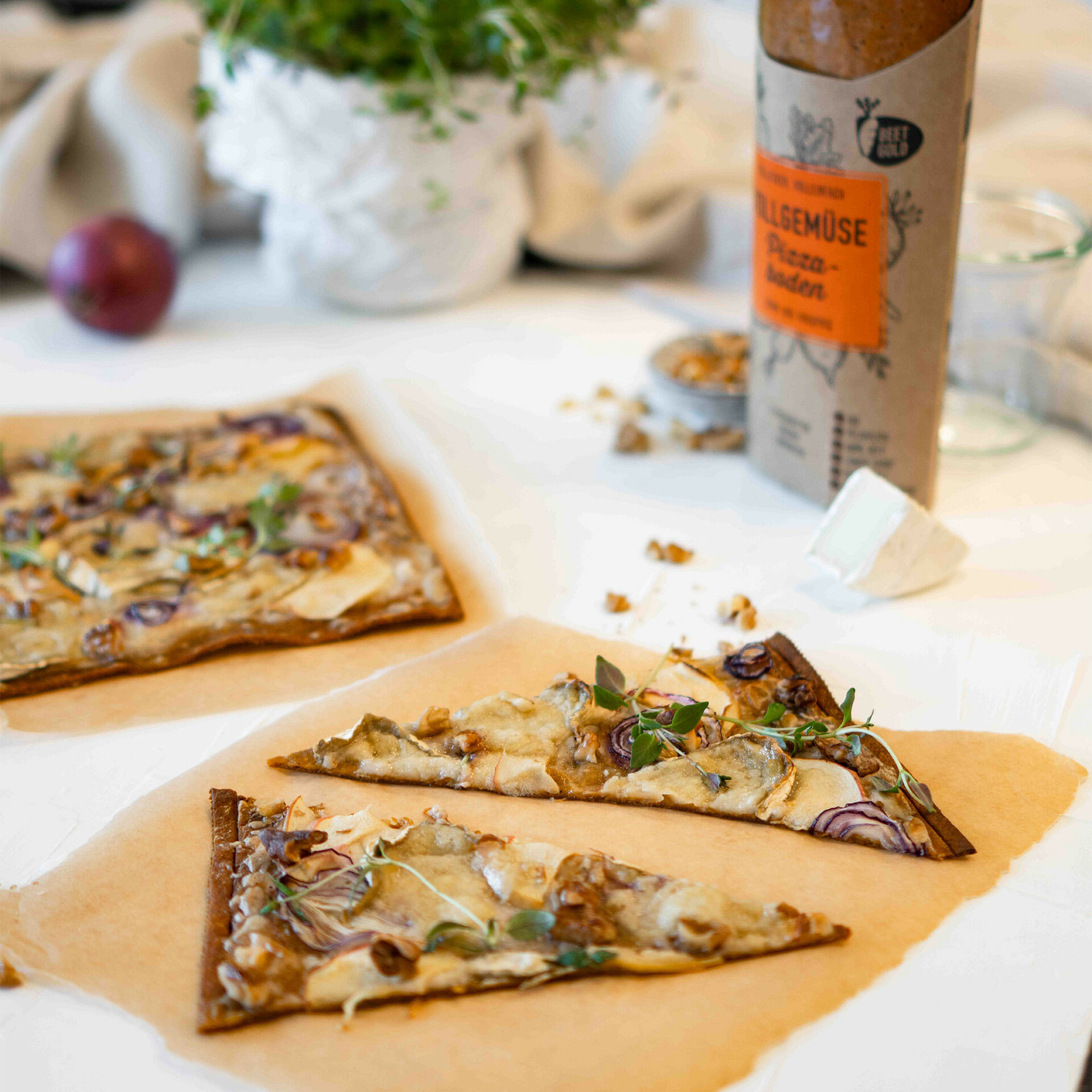 gebackener Pizzaboden als Flammkuchen auf Backpapierabriss, belegt mit Äpfeln, Zwiebeln, Camembert, Walnüssen und Thymian