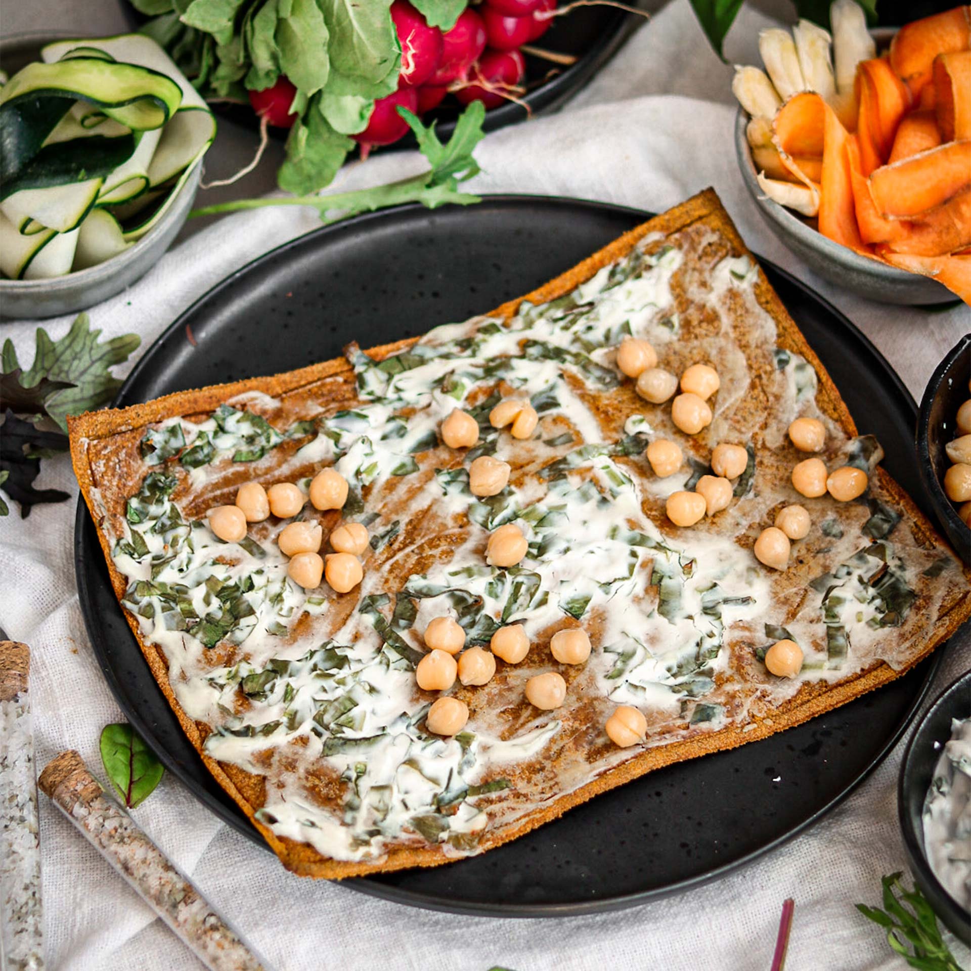 Gebackener Pizzaboden auf schwarzem Teller mit Kräuter Creme Fraîche belegt mit Kichererbsen