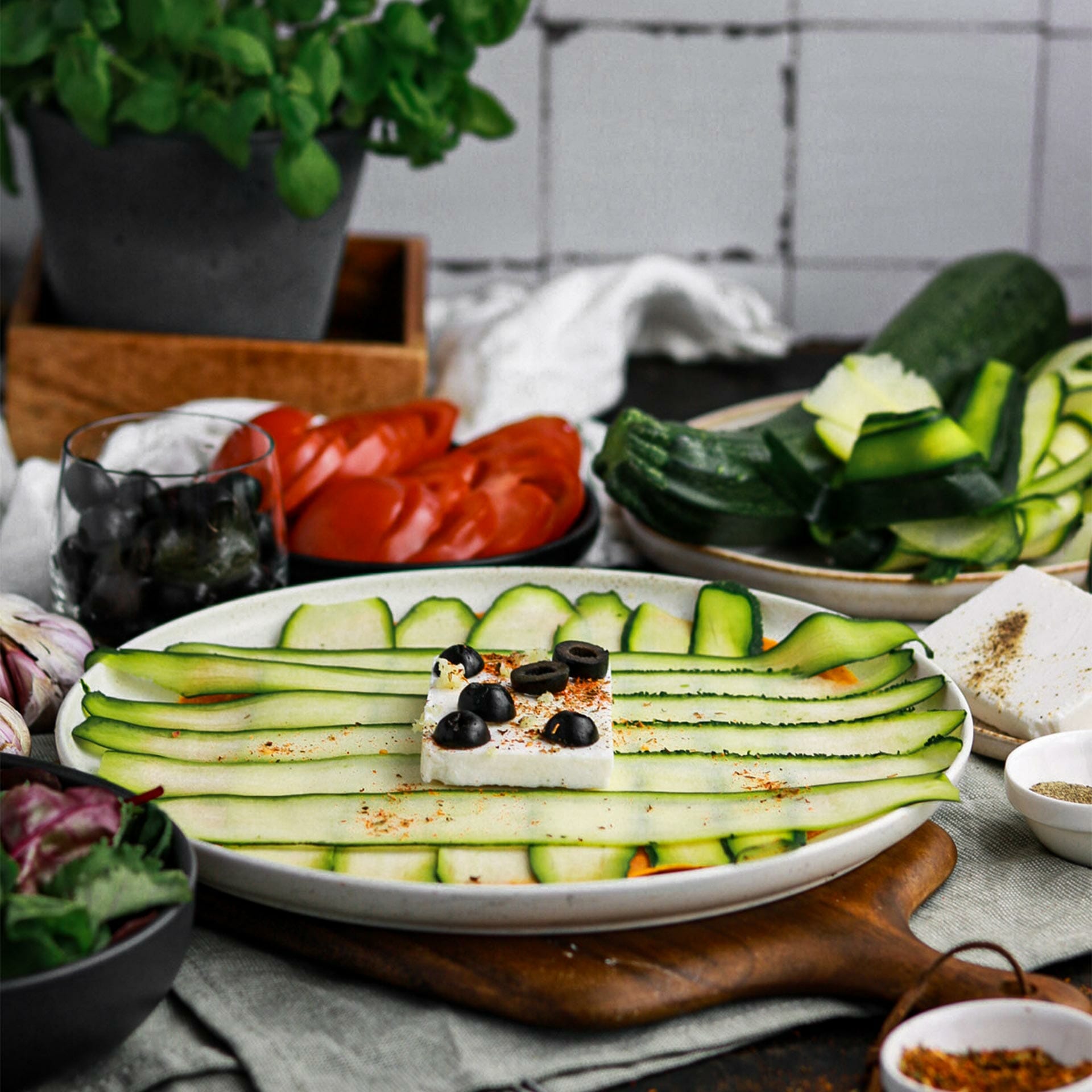 Teller mit Karotten Tortilla belegt mit dünnen Zucchini Streifen, darauf ein Feta Block mit Oliven