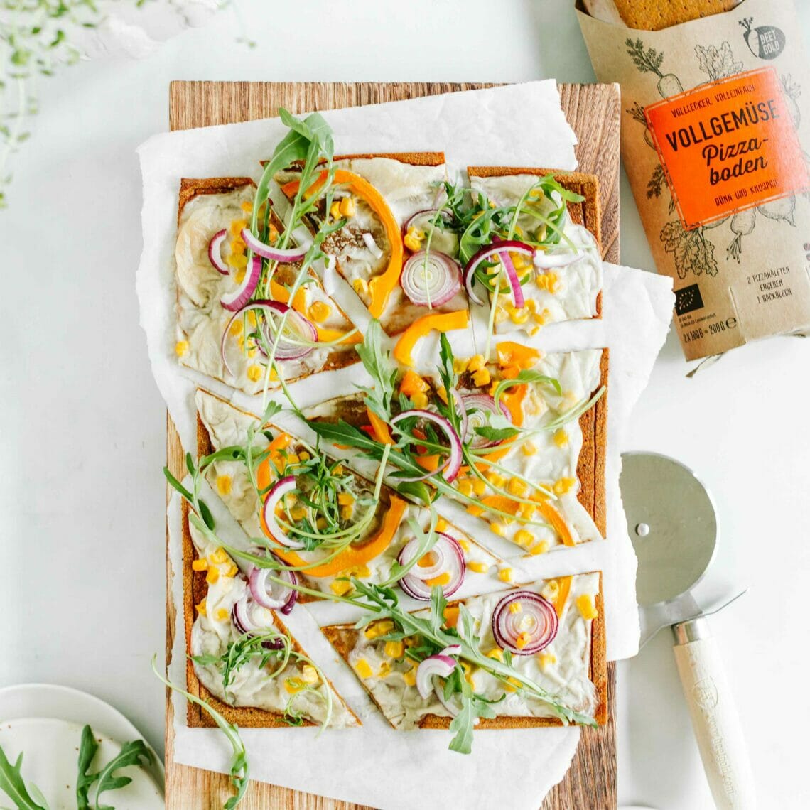 Geschnittener Flammkuchen belegt mit Rucola, Paprika, roter Zwiebel und Mais