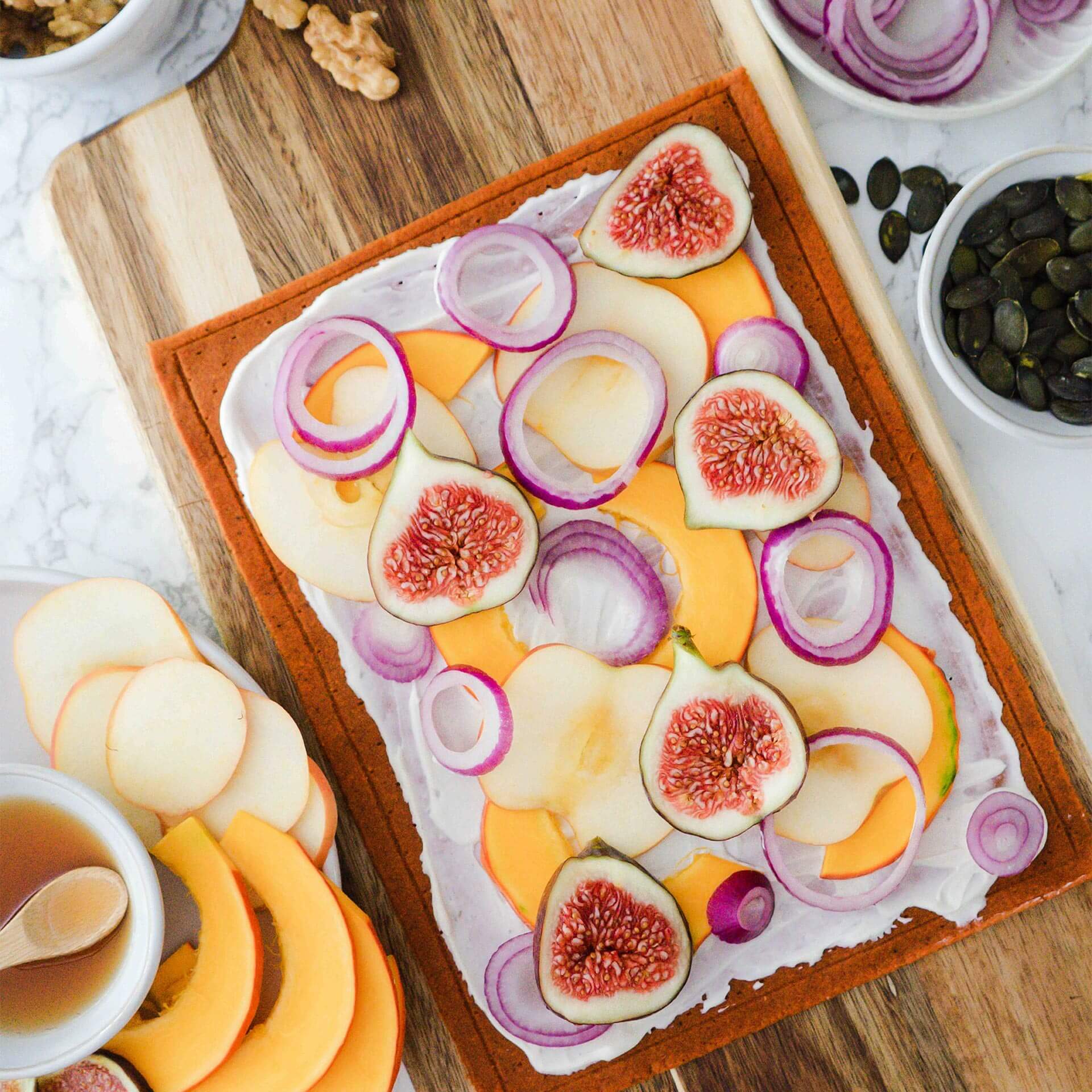 Ungebackener Beetgold Pizzaboden bestrichen mit Creme Fraîche, belegt mit Kürbis, Apfel, Feigen und roten Zwiebeln