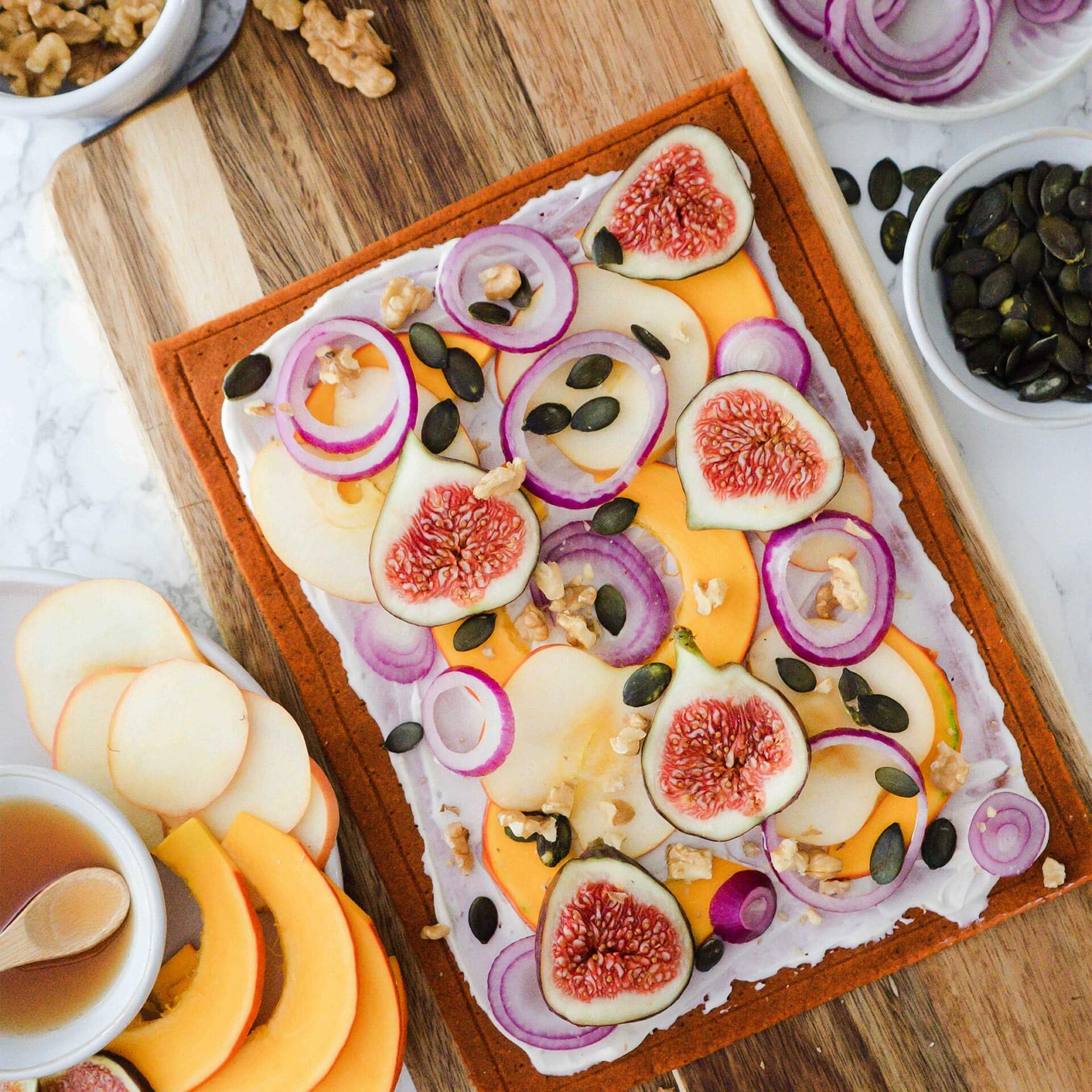 Ungebackener Beetgold Pizzaboden bestrichen mit Creme Fraîche, belegt mit Kürbis, Apfel, Feigen, roten Zwiebeln, Kürbiskernen und Walnusskernen