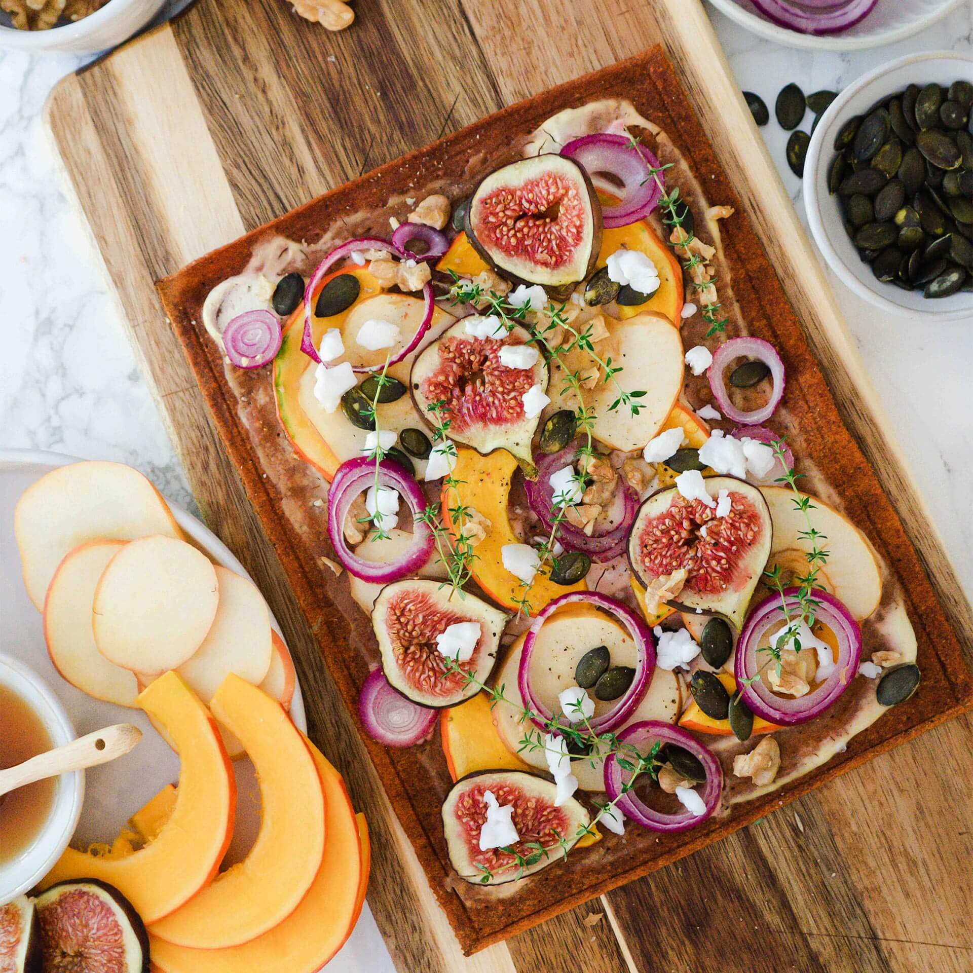 Gebackener Beetgold Pizzaboden als Flammkuchen auf einem Holzbrett, belegt mit Feigen, Zwiebeln Äpfeln, Walnüssen, Kürbiskernen, Thymian und Feta Stücken