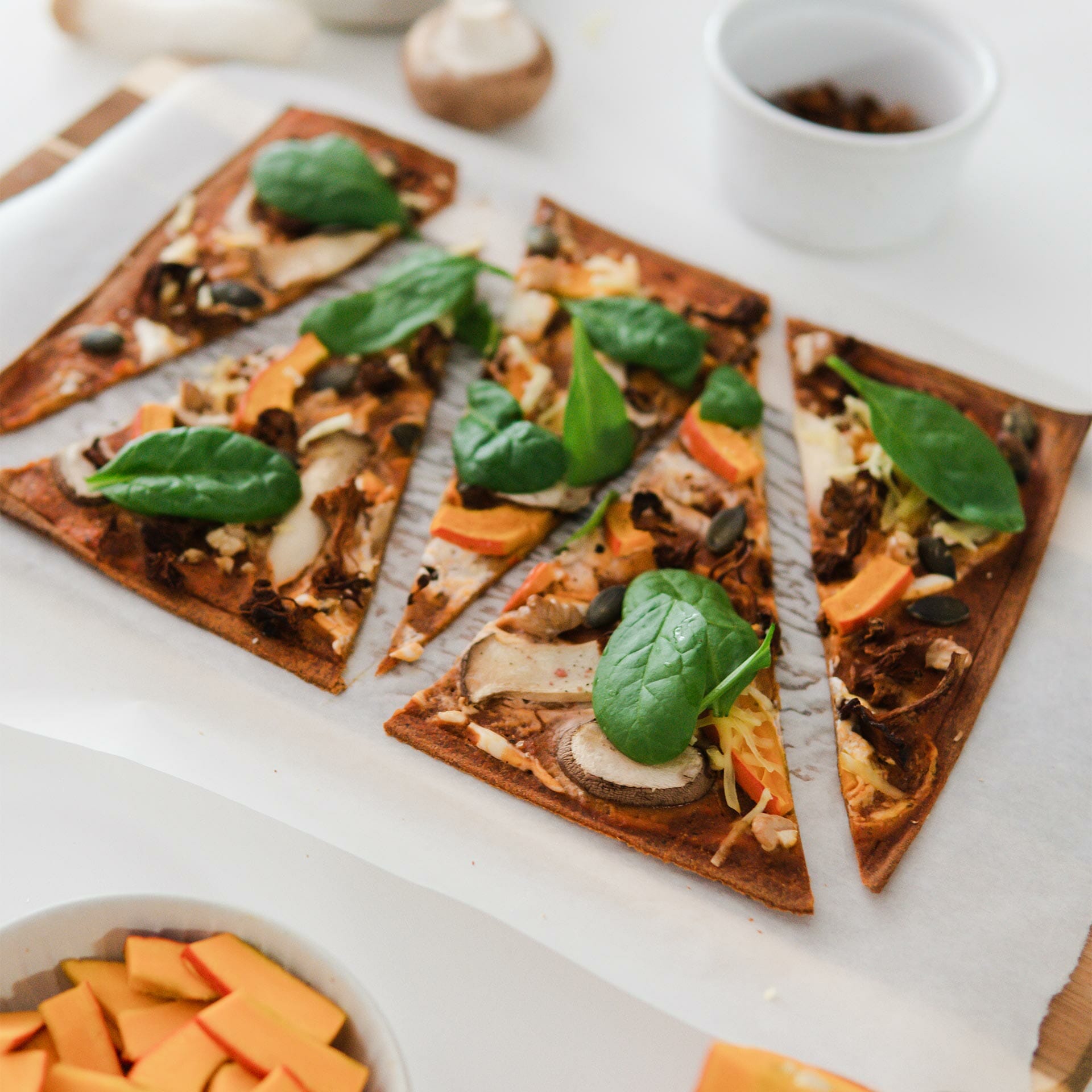 geschnittener Pizzaboden/ Flammkuchen mit verschiedenen Pilzen, Kürbis. Kürbiskernen, Walnüssen und Spinat