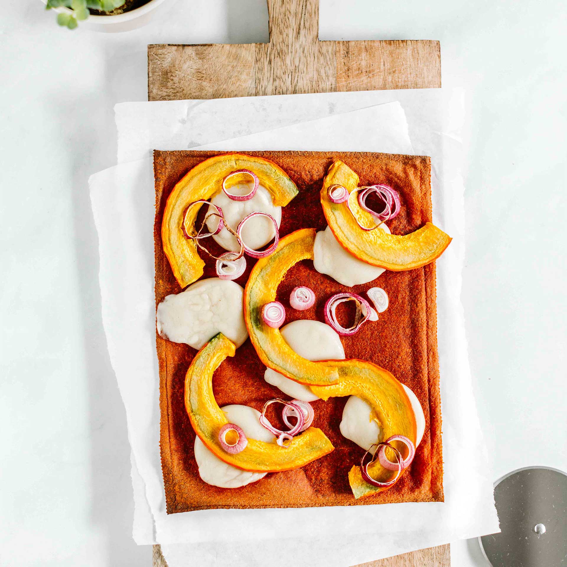 Gebackener Pizzaboden auf Holzbrett belegt mit Mozzarella, Kürbis und Zwiebeln