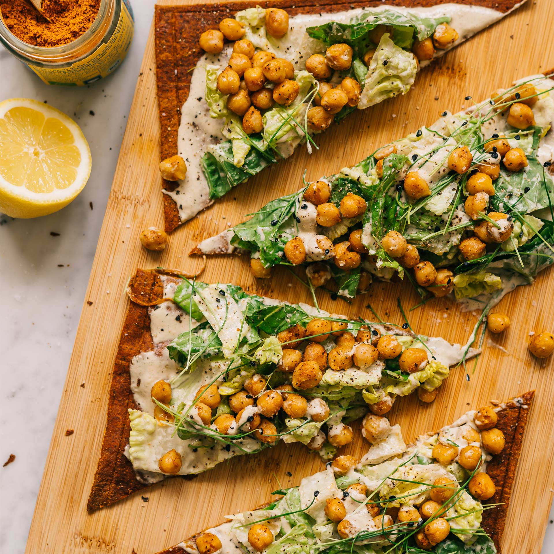 In Dreiecke geschnittener Pizzaboden belegt mit Kicherebsen und Spicy Ceasar Salat