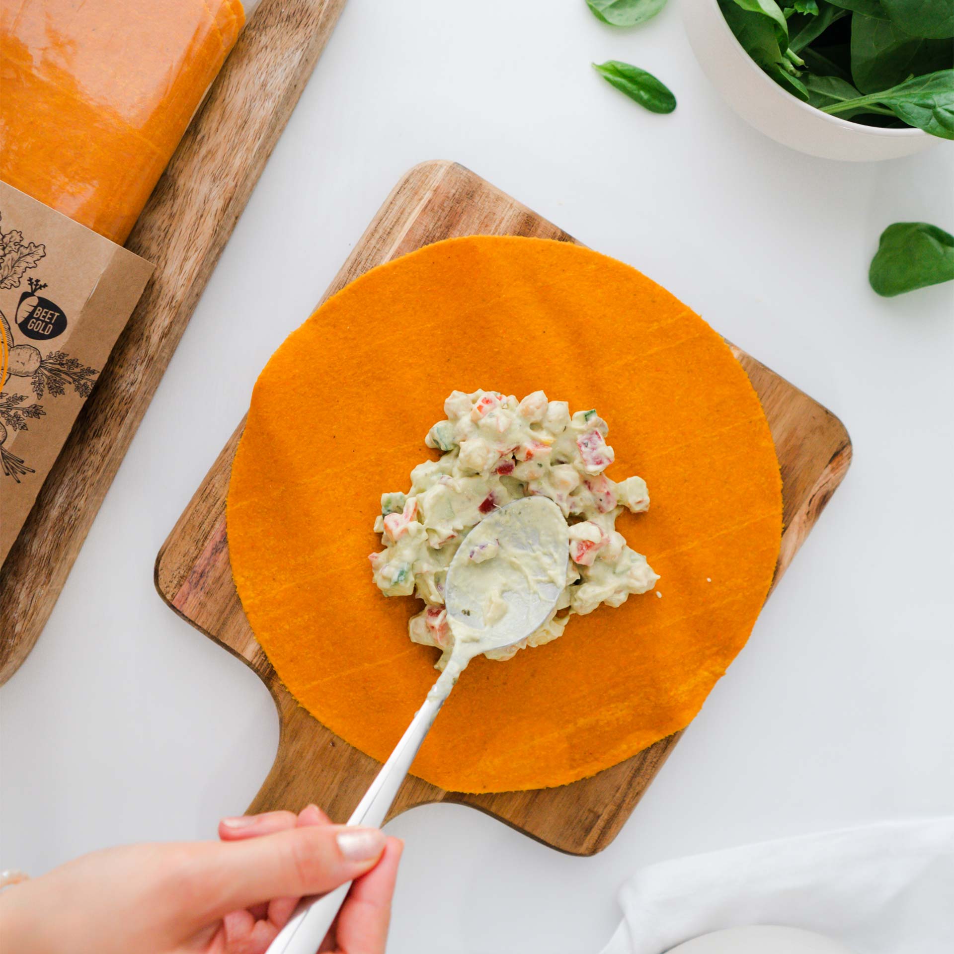Masse aus Gurken, Paprika, Kichererbsen Guacamole und Frischkäse wird mit Löffel auf Karotten Tortilla verteilt